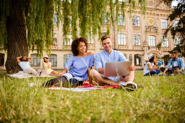E 'piu' facile insieme! Sei compagni di classe allegri sono seduti su un plaid sull'erba verde nel parco primaverile vicino al campus e studiano, si preparano per esami, test, guardano a macchina e sorridono. — Foto Stock