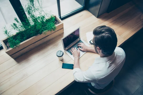 Achteraanzicht van het koelen van jonge hipster luisteren naar de muziek op zijn vakantie in grote witte moderne oortelefoons, in casual jeans slijtage, zitten in een donkere moderne Cafe in de buurt van het venster — Stockfoto