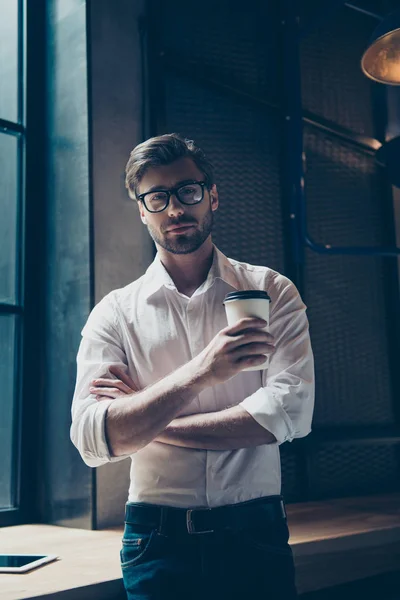 Vista trasera de la escalofriante joven hipster escuchando la música en sus vacaciones en grandes auriculares blancos modernos, en ropa vaquera casual, sentado en un café moderno oscuro cerca de la ventana — Foto de Stock