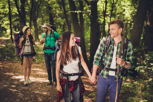 Cuatro amigos emocionados los turistas están caminando en el bosque de otoño, hablando y disfrutando, vistiendo trajes cómodos para hacer senderismo, tomados de la mano, dos parejas encantadoras —  Fotos de Stock