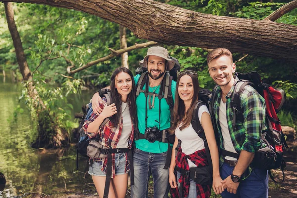 Primer plano de cuatro amigos alegres en el bosque agradable verano. Son turistas en vacaciones, posando para el retrato en una selva soleada de verano —  Fotos de Stock