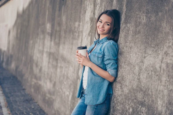 Charmiga drömmande unga Brunett Söt tjej dricker varmt te nära betongväggen utomhus. Hon är sömnig och avslappnad, i casual jeans kläder — Stockfoto