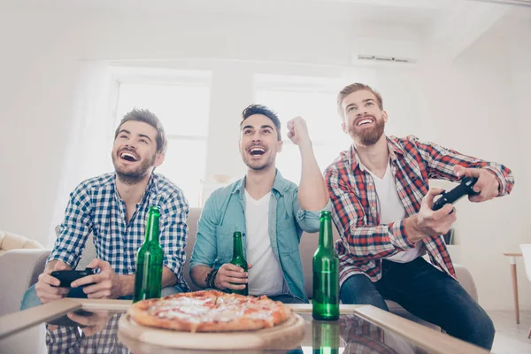 ¿Sí? ¡Equipo de ganadores! La vida de un hombre soltero. Bajo ángulo de tres hombres felices y alegres, sentados en el sofá y jugando videojuegos con cerveza y pizza, sonriendo, haciendo gestos, disfrutando — Foto de Stock