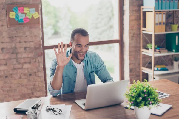 Hey daar! Jonge vrolijke afro Amerikaanse jongen is zwaaien in de camera terwijl het hebben van video-oproep zittend op zijn werkplek in casual kleding thuis — Stockfoto