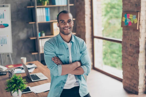 Portret van succesvolle zwarte kerel, kijken naar de camera, permanent met gekruiste armen op zijn werkplek op kantoor, in casual smart, glimlacht — Stockfoto