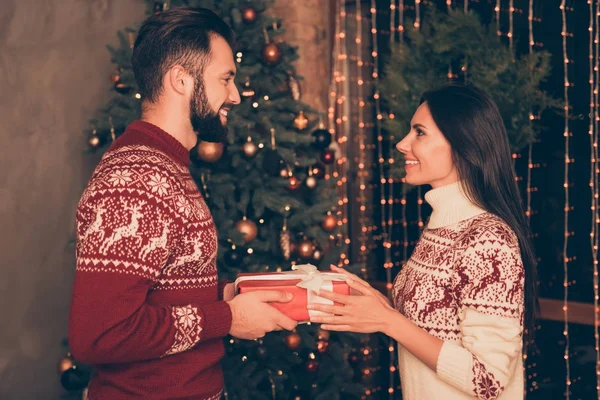 Süße Eheleute erhalten Geschenke mit weißer Schleife, zu Hause drinnen, so aufgeregt, in gestrickten, niedlichen traditionellen Weihnachtskostümen mit Ornamenten, genießen, Tanne, Winter — Stockfoto