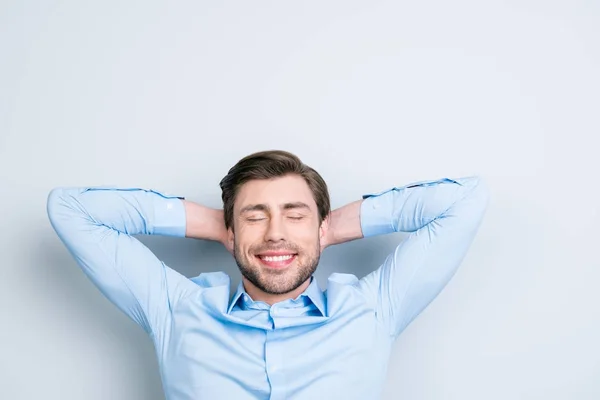 Tempo para relaxar.Close-up retrato de bonito jovem sonhando homem com os olhos fechados de mãos dadas atrás de sua cabeça tendo tempo-out enquanto em pé sobre fundo cinza — Fotografia de Stock