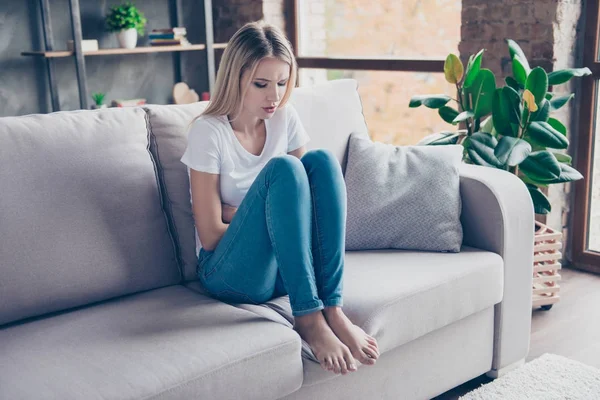 怒っている女性は、月経前緊張症の最初の症状を持っています。彼女はソファに座ってください。 — ストック写真