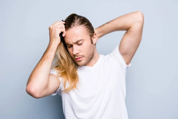 Beau concentré jeune homme en vêtements décontractés peigne son — Photo