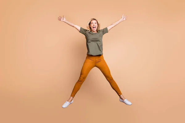 Foto de comprimento total de senhora funky louco pulando alto fazendo figura forma de estrela gastando melhor tempo livre desgaste verde t-shirt calças amarelas tênis isolado cor bege fundo — Fotografia de Stock