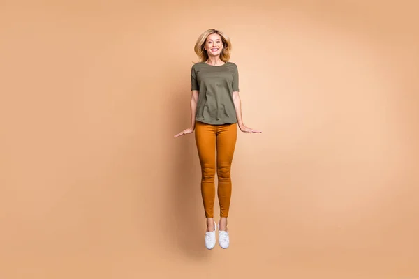 Full length photo of crazy lady jumping wysoki podekscytowany letni nastrój nowoczesny wygląd nieśmiały osoba nosić zielony t-shirt żółte spodnie trampki izolowane beżowy kolor tła — Zdjęcie stockowe