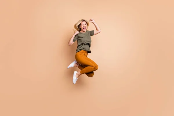 Full length profile photo of crazy lady jumping high competitive mood celebrating καλύτερη νίκη θριαμβευτική φθορά πράσινο t-shirt κίτρινο παντελόνι απομονωμένο μπεζ χρώμα φόντο — Φωτογραφία Αρχείου