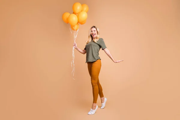 Full length profile photo of charming blonde lady holding many bright orange air balloons came halloween party wear green t-shirt παντελόνι απομονωμένο μπεζ χρώμα φόντο — Φωτογραφία Αρχείου