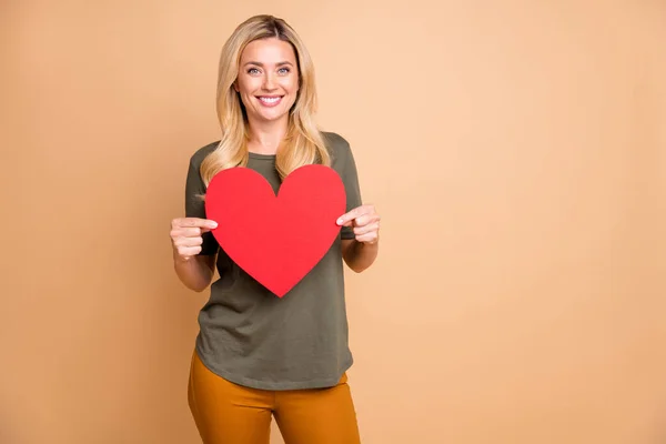 Foto von fröhlichen positiven niedlich hübsch attraktive Frau hält großes rotes Herz trägt gelbe Hose grüne Hose lächelnd zahnlos in der Nähe leeren Raum isoliert pastellfarbenen Hintergrund — Stockfoto