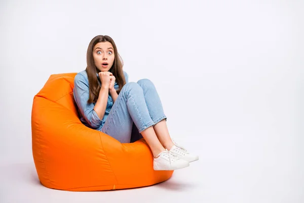 Full size photo of scared girl sit big lounge chair watch horror series feel nervous have shock stay speechless voiceless wear denim jeans outfit sneakers isolated white color background — Stok fotoğraf