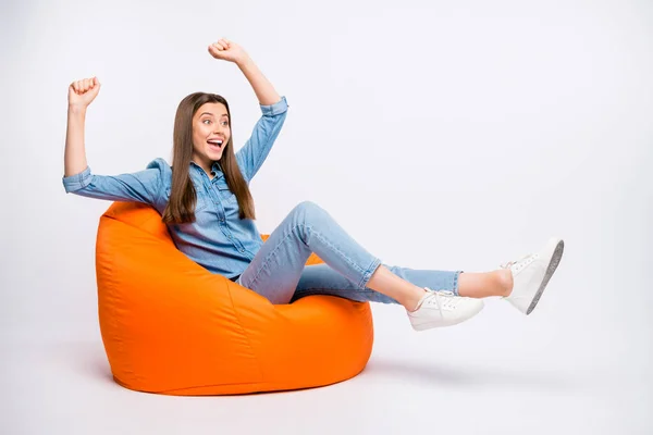 Yeah we win. Full size profile side photo of amazed crazy girl sit bag armchair watch football match see victory impressed raise fists scream omg wear denim jeans isolated over white color background — 图库照片