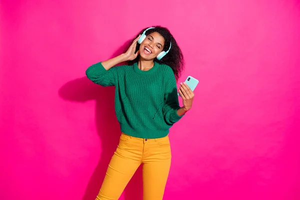 Portret van vrolijk positief meisje met headset gebruik smartphone luisteren stereo melodie lied zingen op herfst vakantie dragen groene trui geel trendy broek geïsoleerde roze kleur achtergrond — Stockfoto