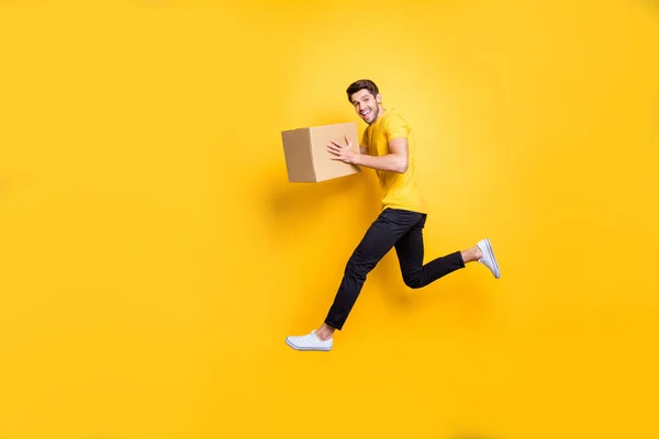 Full size foto di bel ragazzo che salta alta tenuta pacco casella fretta spostare nuovi appartamenti trasporto indossare casual t-shirt pantaloni isolato colore giallo sfondo — Foto Stock