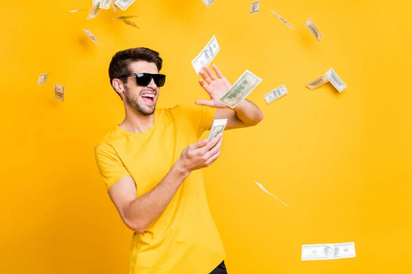 Foto von jungen hübschen unvorsichtigen Kerl werfen Geld Banknoten weg wohlhabende Person tragen Sonne Spezifikationen lässig T-Shirt isoliert helle gelbe Farbe Hintergrund — Stockfoto