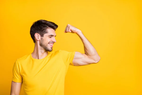 Photo of young handsome guy holding fist raised demonstrating perfect big biceps result after new sport gym wear casual t-shirt isolated yellow color background — ストック写真