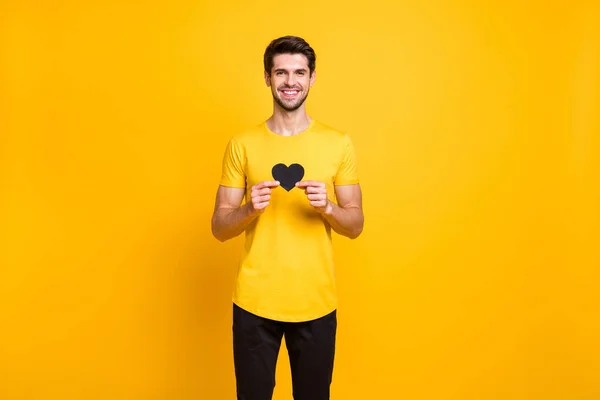 Portrait of his he nice attractive cheerful cheery affectionate guy holding in hands small little black heart like human healthcare isolated over bright vivid shine vibrant yellow color background — ストック写真