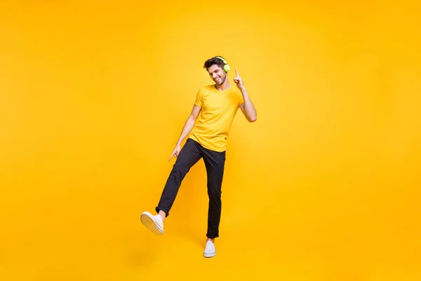 Full length foto van knappe jongen op studenten feest luisteren jeugd muziek oorkleppen dansen jong beweegt dragen casual t-shirt broek geïsoleerde gele kleur achtergrond — Stockfoto