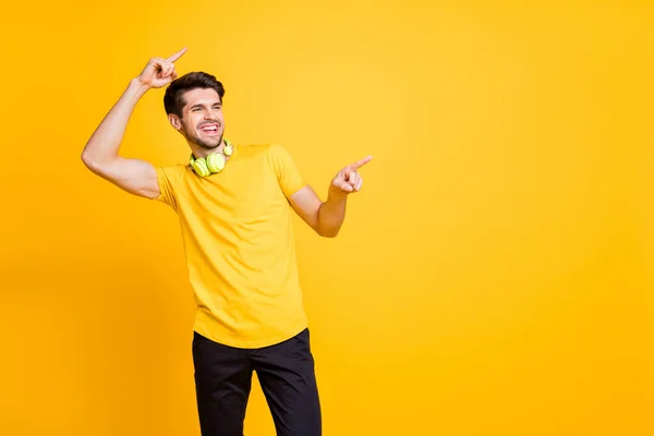 Photo of youngster handsome guy students party listening cool music earflaps indicating fingers empty space wear casual t-shirt pants isolated yellow color background — Stock Fotó