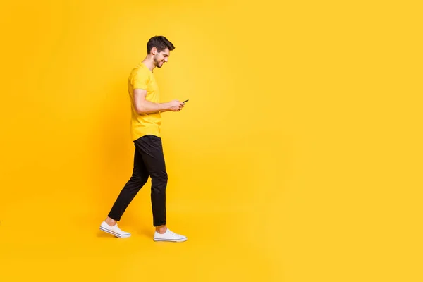 Tamanho total do corpo foto de homem atraente alegre com cerda sorrindo toothily focado na leitura feednews em seu telefone vestindo amarelo t-shirt calçado branco isolado fundo de cor brilhante — Fotografia de Stock