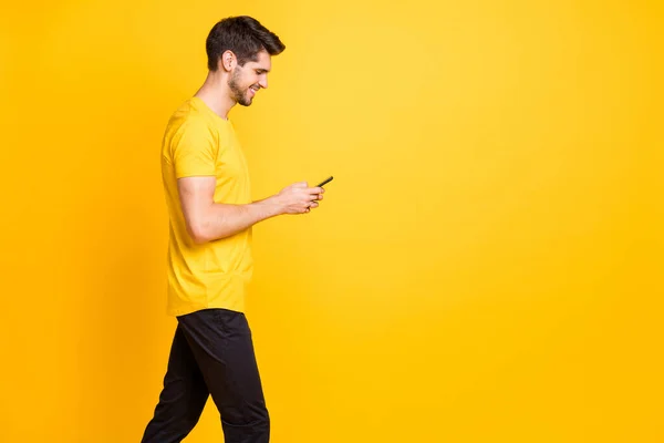 Zdjęcie radosnego, modnego, przystojnego, atrakcyjnego mężczyzny uzależnionego od przeglądania profilu w mediach społecznościowych, noszącego koszulkę w czarnych spodniach, odizolowane, żywe tło koloru — Zdjęcie stockowe