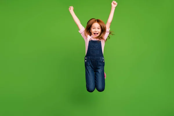 明るいかわいい小学生ジャンプ高喜び夏休み週末カジュアルデニム全体ピンクシャツ隔離された緑の背景を身に着けている — ストック写真