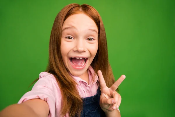 Κοντινή φωτογραφία του όμορφη μικρή αλεπού κυρία δείχνει σύμβολο v-σημάδι κάνοντας selfies ενθουσιασμένοι χαρούμενη διάθεση φορούν denim συνολικά ροζ πουκάμισο απομονωμένο πράσινο φόντο — Φωτογραφία Αρχείου