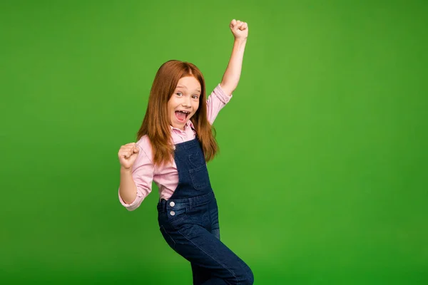 Profile photo of little ginger schoolchild celebrating winning classmates team in sportive competitions raise fists wear denim overall pink shirt isolated green background — Φωτογραφία Αρχείου