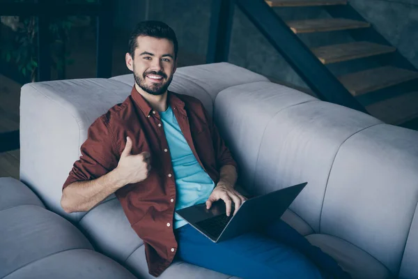 Gran trabajo. Retrato de chico alegre positivo mentira en el trabajo de diván utilizar su ordenador portátil mostrar pulgar hacia arriba aprobar ropa de trabajo interior ropa de estilo casual en la oficina moderna loft —  Fotos de Stock