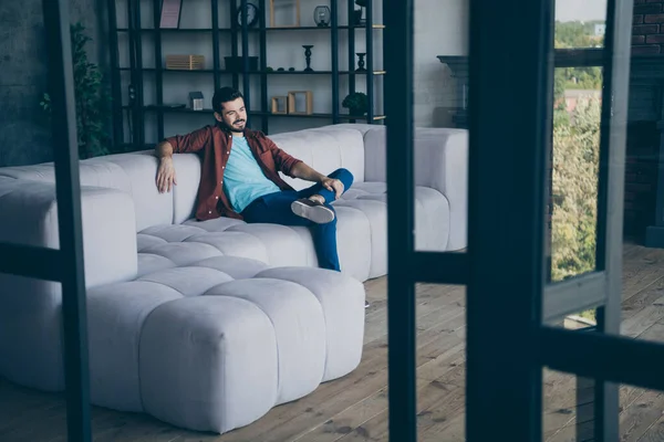 Фото красивого хлопця у вітальні, що сидить зручний диван розслабляє суботній вечір, тримаючи ногу на колінах сучасної квартири в приміщенні повсякденного одягу — стокове фото