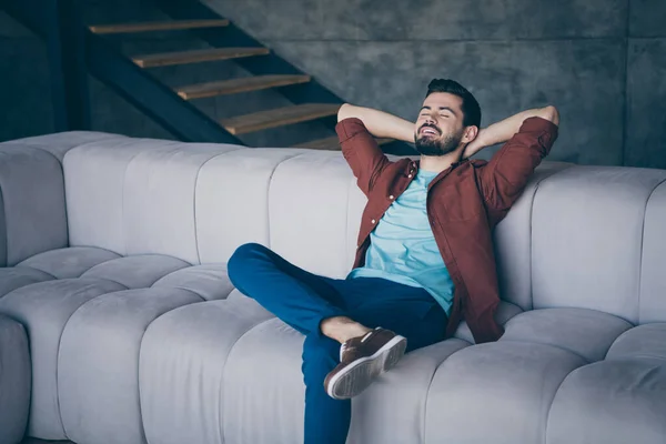 Fotografie pohledný chlap v high spirits drží ruce za hlavou sedí pohodlný velký gauč spí relaxační sobotní ráno v moderním bytě podkroví vnitřní — Stock fotografie