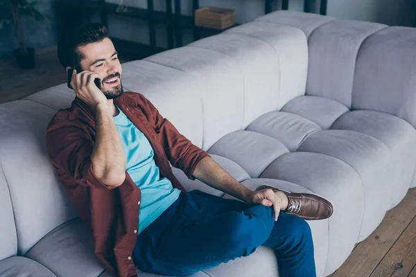Foto de perfil de chico guapo sosteniendo teléfono cerca de la oreja escuchando amigo extranjero chatterbox acogedor sentarse sofá en la sala de estar apartamento moderno interior casual vestido — Foto de Stock