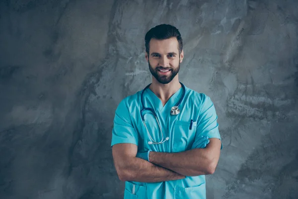 Zdjęcie wesoły pozytywny przystojny lekarz z ramionami skrzyżowane uśmiecha się zbyt mocno pokazując swoją wiedzę w medycynie odizolowany szary mur beton tło — Zdjęcie stockowe