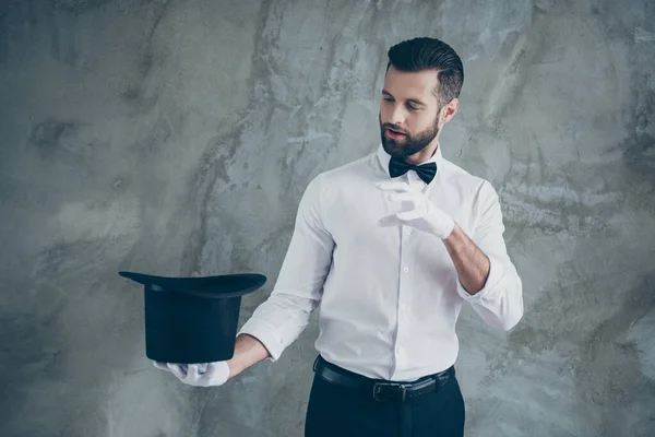 Foto von professionellen Illusionist vorgibt, einen Bann zu ziehen, um etwas aus seinem zylindrischen Hut isoliert über graue Wand Betonhintergrund zu nehmen — Stockfoto