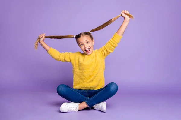 Foto de comprimento total de conteúdo alegre criança sentar cruzado pernas dobradas se divertir nos fins de semana segurar seus rabos de cavalo usar roupa de estilo casual isolado sobre fundo cor violeta — Fotografia de Stock