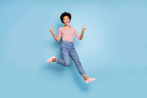 Gedraaide full length body size foto van vrolijke positieve leuke mooie vriendin running springen tonen dubbele v-teken in jeans denim gestreept shirt krullend golvend geïsoleerde pastel blauwe kleur achtergrond — Stockfoto