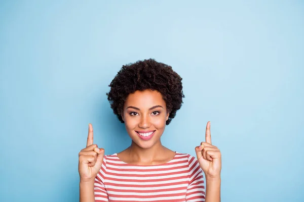 Closeup photo of pretty dark skin lady indicating fingers up empty space advising buyers new amazing products wear striped shirt isolated blue color background — ストック写真