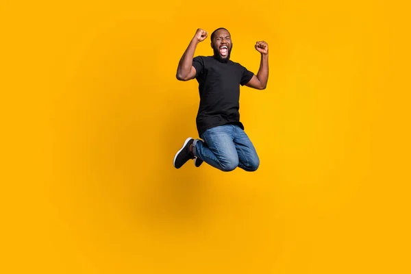 Sim, ganhei. Foto em tamanho completo de encantado engraçado louco afro americano cara comemorar loteria vitória salto levantar punhos gritar desgaste t-shirt jeans jeans isolado cor brilhante fundo — Fotografia de Stock