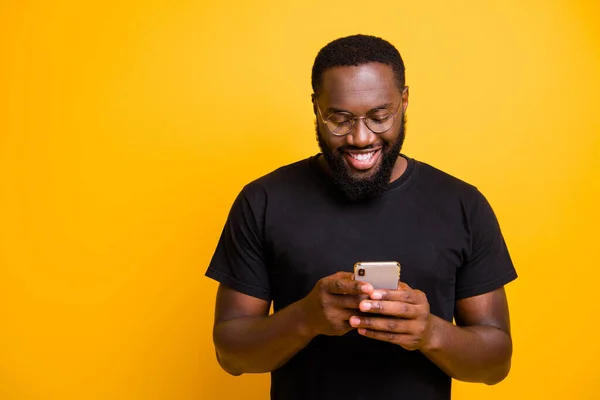Фото веселого зубастого сияющего черного человека, просматривающего свой телефон в поисках новой информации в очках изолированного яркого цвета фона — стоковое фото