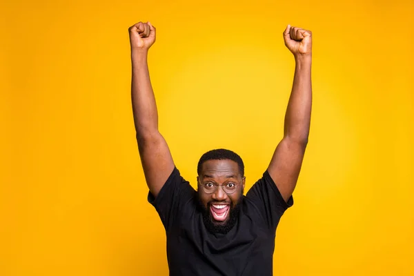 Photo of excited overjoyed rejoicing man expressing crazy emotions on face in eye glasses raising his fists up after winning tickets to go abroad on vacation isolated vivid color yellow background — Zdjęcie stockowe