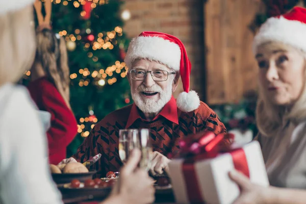 Phot av farfar positiv glad leende i glasögon glasögon bär Santa hatt huvudbonad känsla festlig stämning i samtal med gäster — Stockfoto