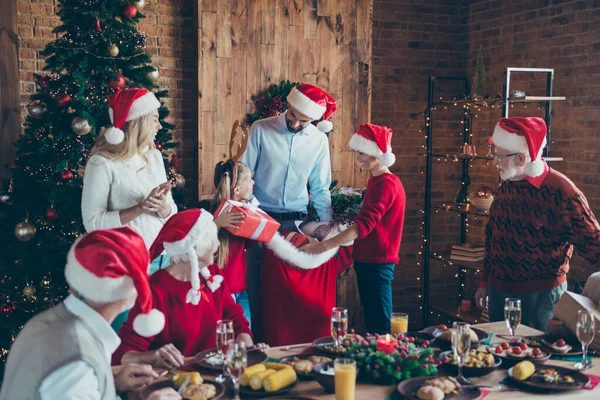 Neşeli, pozitif, büyük bir ailenin fotoğrafı. Babaları, erkek ve kız kardeşlerine hediyeler veriyor. Birkaç kuşak boyunca Noel Baba şapkalarıyla gülümsüyor. — Stok fotoğraf
