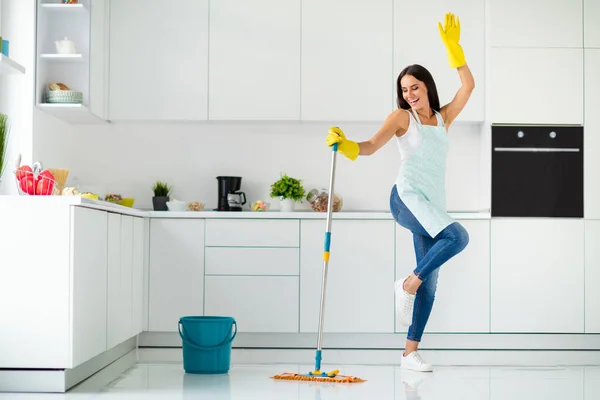 Full length photo of crazy cheerful gilr wash floor in kitchen with mop want have relax fun imagine she dances clubbing raising hands screaming wearing dotted apron indoors