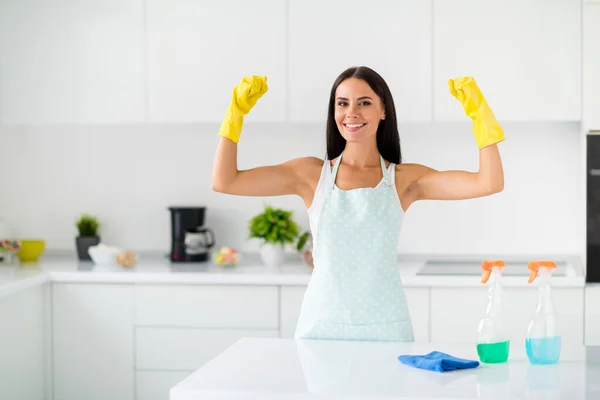 Superhero for dirty rooms. Brunetthair girl wearing yellow rubber gloves show muscles advertise she can clean wash polish all furniture in kitchen indoors