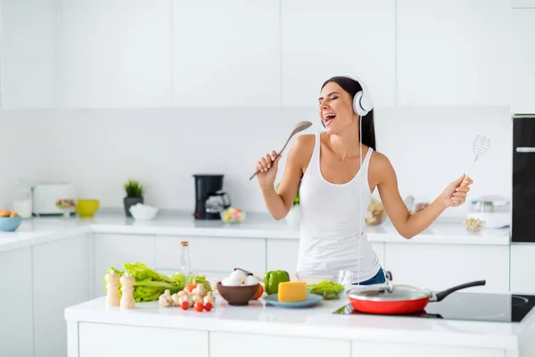 Портрет фанки веселой домохозяйки представьте, что она поп начать слушать музыку на наушниках держать кухонную утварь петь любимую песню во время приготовления ужина вкусный обед в белом доме — стоковое фото