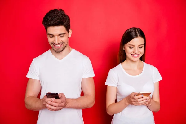 Фото веселой брюнетки рыжеволосой зубастой сияющей пары, беседующей друг с другом, довольной новым подключением к интернету в белой футболке, изолированной с телефонами ярким цветовым фоном — стоковое фото